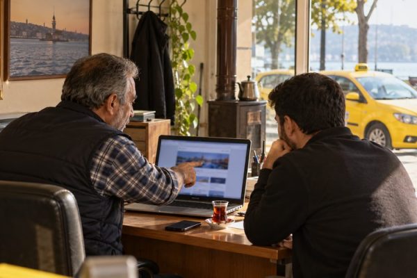 Taksi durağında bilgisayardaki site bilgilerini birlikte inceleyen iki kişi