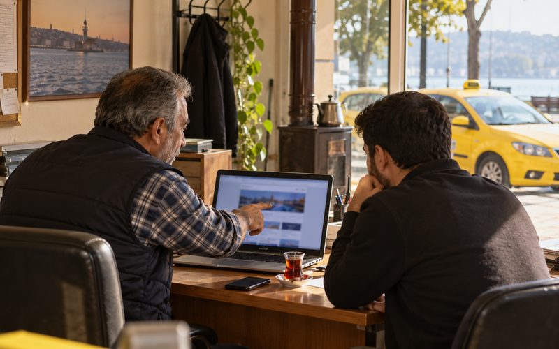 Taksi durağında bilgisayardaki site bilgilerini birlikte inceleyen iki kişi